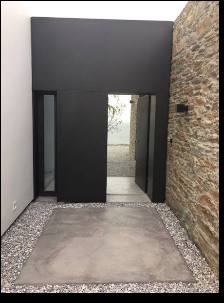 Είσοδος κατοικίας με μαύρη μεταλλική πόρτα και πέτρα